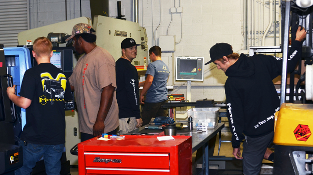 MetalCloak employees in machine shop wearing branded black sweatshirt and longsleeve t-shirt and tan shirt