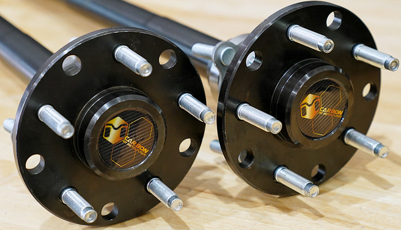 pair of black vehicle axles with silver bolts and gold and carbon fiber Carbon by MetalCloak badges in center