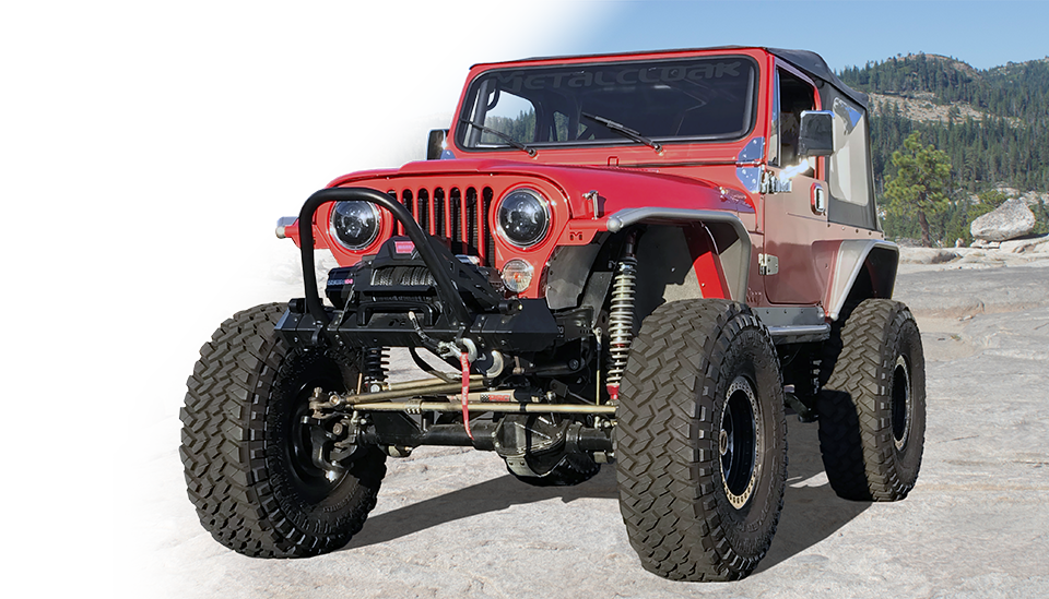 Red Jeep CJ driving on granite rock slab with red and silver MetalCloak fenders and gold suspension, with alpine trees in background