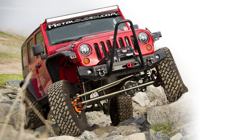 red Jeep JK Wrangler with gold plated control arms and suspension and black MetalCloak fenders navigating large boulders on an outdoor grassy trail