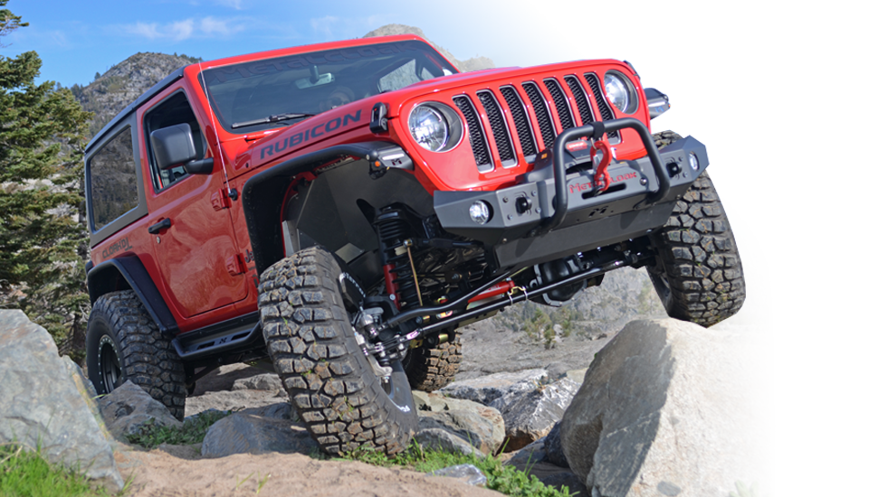 red Jeep JL Wrangler with black control arms and tie rods and tow winch climbing over large boulders on the Rubicon Trail with alpine trees and mountains behind it