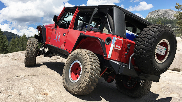 red JK Wrangler with silver MetalCloak decal and black powdercoat fenders and rear bumper and skid plates on a granite alpine trail on the Rubicon with trees and mountain ridges