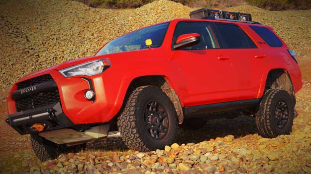 red Toyota FJ Cruiser with roof rack and tow hitch crawling over large gravel and rocks on a hillside